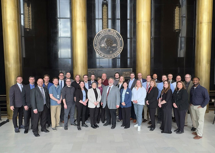 A large group of NDIT team members gather for a group photo under the state seal at the North Dakota Capitol.