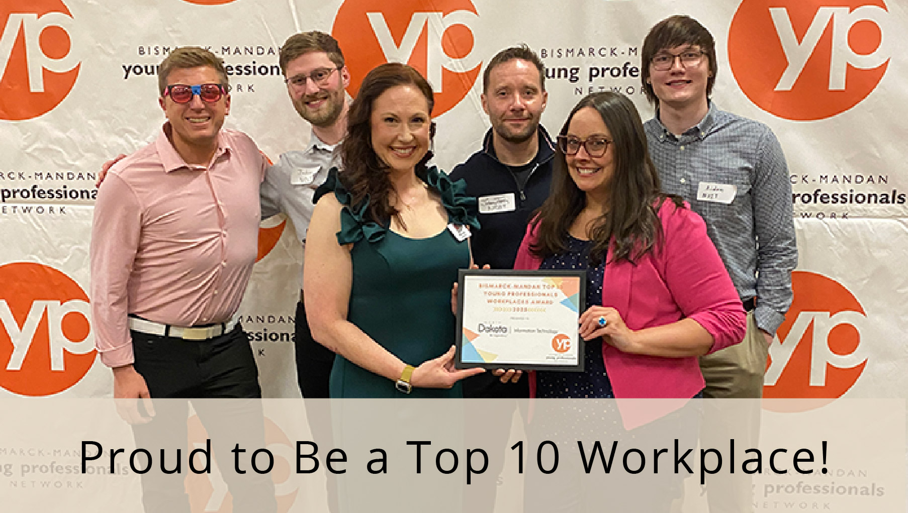Six excited NDIT team members gather around a plaque, with overlaying text that says we're proud to be a top 10 workplace.