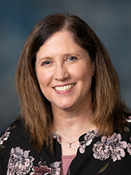 A professional headshot of Evonne Amundson wearing a dark shirt with a light flower pattern in front of a charcoal backdrop.