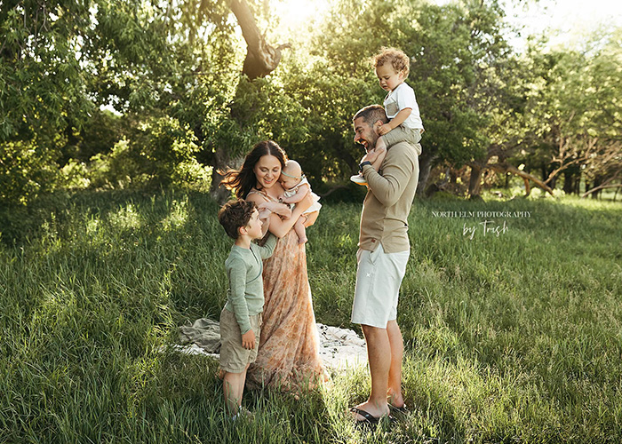 A portrait of Raulie Berthold, her husband, and their three kids—two little boys and a baby girl—outdoors on a sunny day.