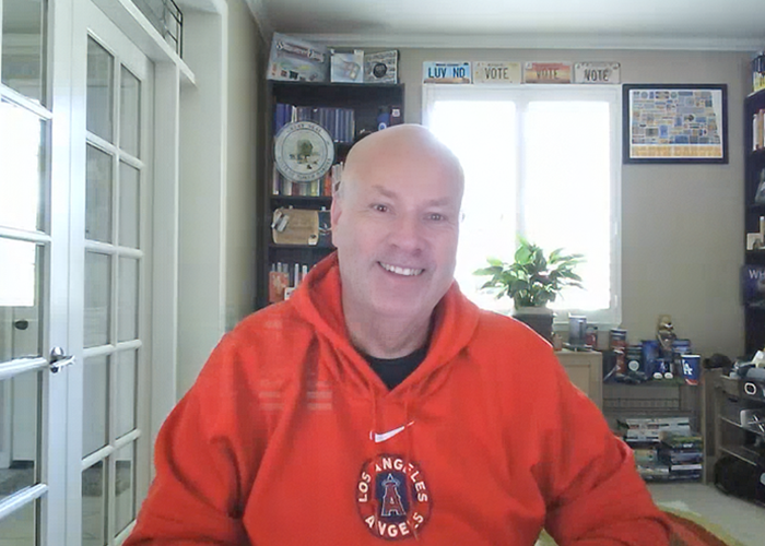 Brian Newby smiles and wears a red Los Angeles Angels hoodie while on a video call in his California home office.
