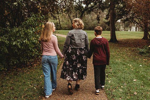 Jessy Wetsch walks happily down an outdoor path with her daughter at her left and her son at her right.