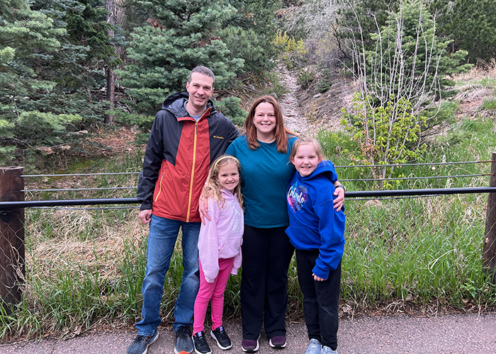Josh Kadrmas, his wife, and their two young girls happily pose for a picture in front of a scenic ravine. 