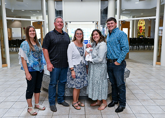 Lyle Ripplinger poses for a family picture in front of a baptismal fountain in a well-lit church.