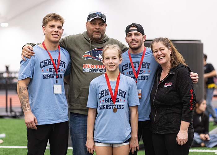 Tina Radenz, her husband, their two grown sons, and young daughter pose at a wrestling meet, where their team earned medals.
