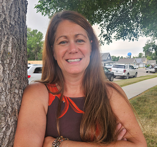 Senior Information Security Officer Tina Radenz smiling and folding her arms while leaning against a tree on a beautiful day.