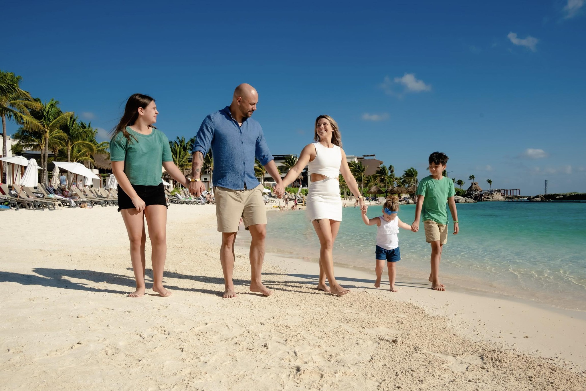 Jared Lemieux happily walking hand-in-hand with his wife and three kids on a sunny, sandy beach near the ocean.