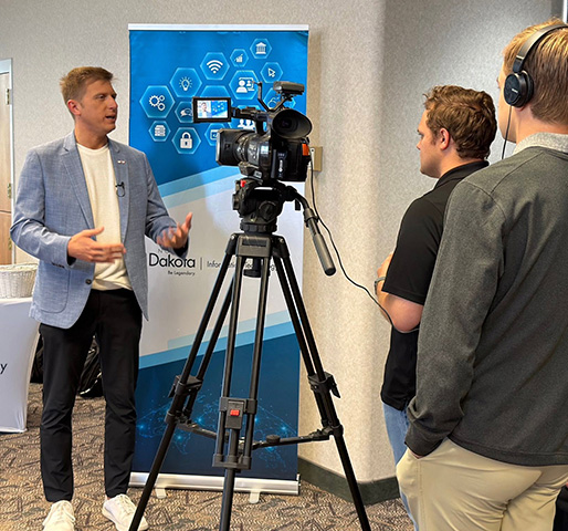 CIO Corey Mock in front of a news camera doing and interview with two other men.