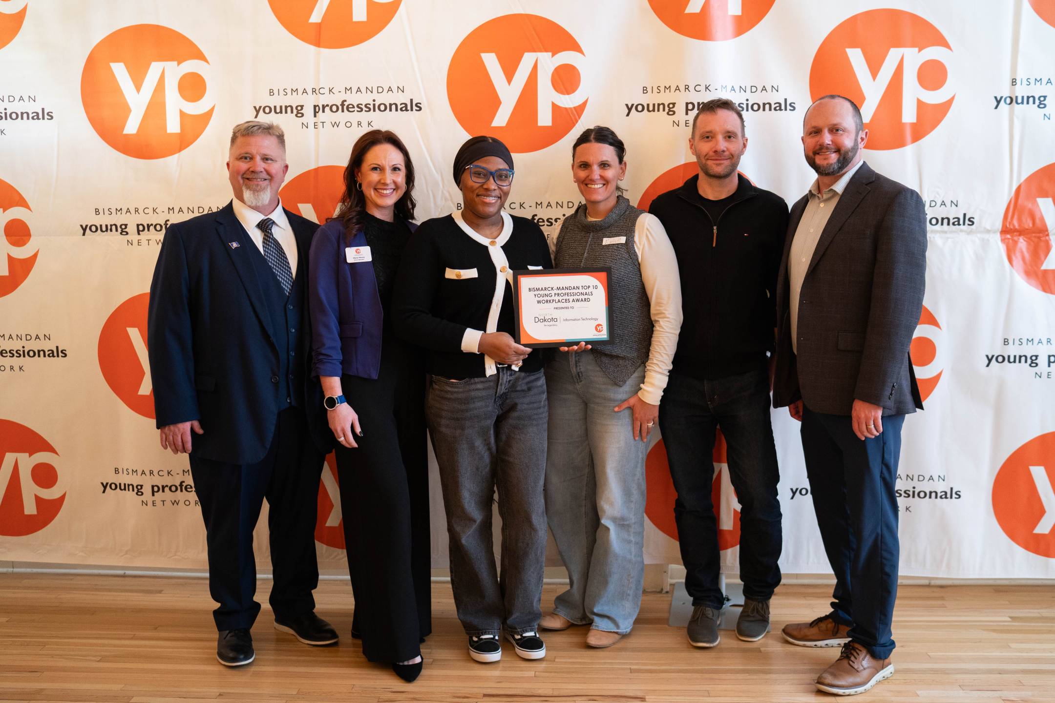 NDIT team members stand together in front of a Bismarck-Mandan Young Professionals Network backdrop, with one team member holding an award certificate.