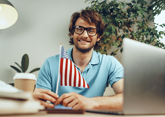 Man with glasses and a blue polo shirt sitting at a desk with an American flag.