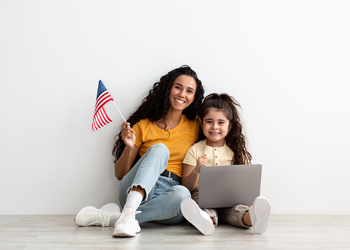 Mother and daughter sitting with a laptop on the floor, mom is holding and American flag.
