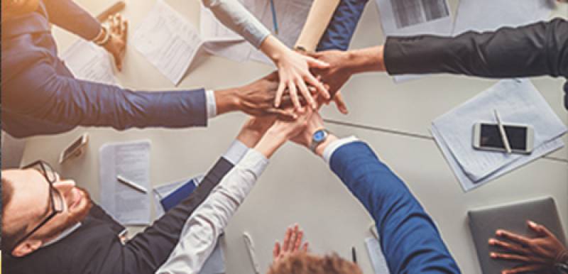 Five business professionals joining hands to symbolize teamwork.