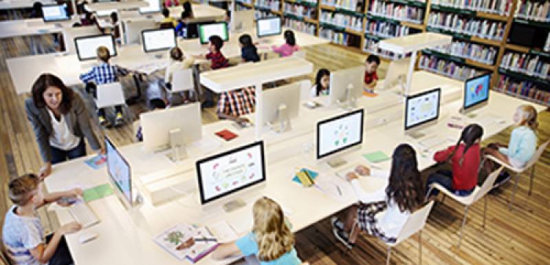 Multiple kids seated around a large desk looking at individual monitors.