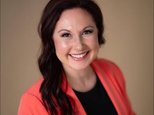 A professional headshot of Dana Henry a caucasian woman with long black hair, wearing a black shirt and red blazer.