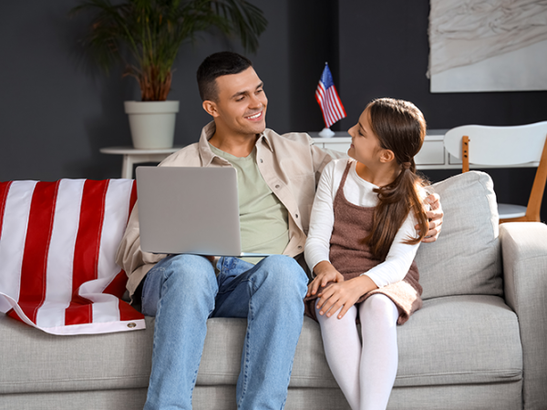 Dad and daughter sitting on a couch with a laptop.