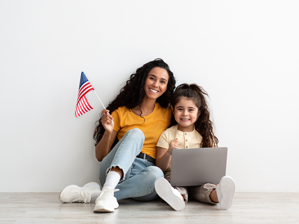 Mother and daughter sitting with a laptop on the floor, mom is holding and American flag.
