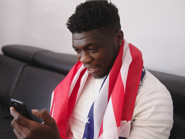 African American male sitting on a couch with a cell phone.