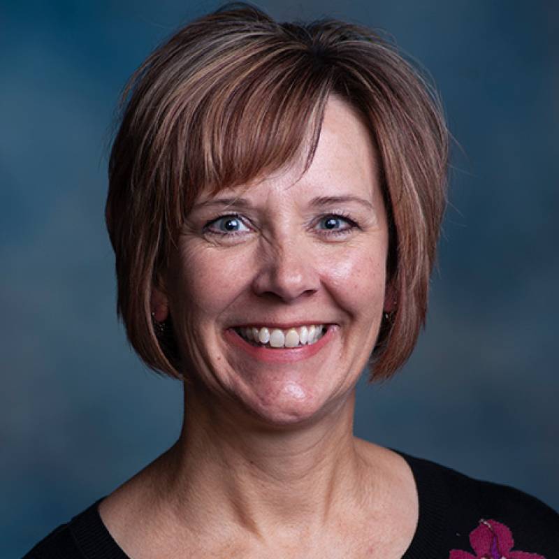 A professional headshot of Kim Weis in front of a blue backgroud.