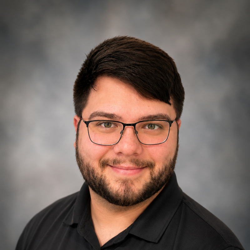 A professional headshot of Skyler Lunsford wearing a black polo shirt and glasses