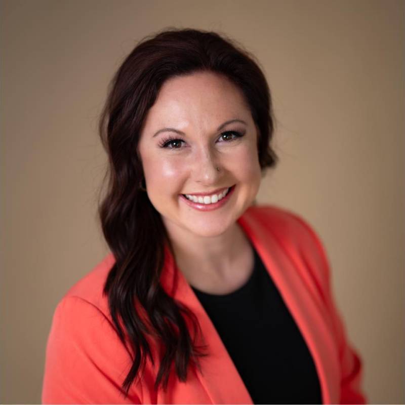 A professional headshot of Dana Henry a caucasian woman with long black hair, wearing a black shirt and red blazer.