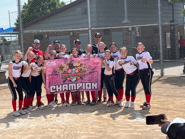 Andrew Sherwood stands with his daughter’s softball team and a championship banner on a sunny day after clinching a victory