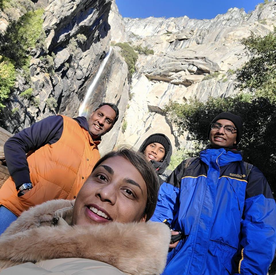 Ravi Shivdat’s wife taking a selfie with him and their two sons in front of a rockface and waterfall on a cold, clear day