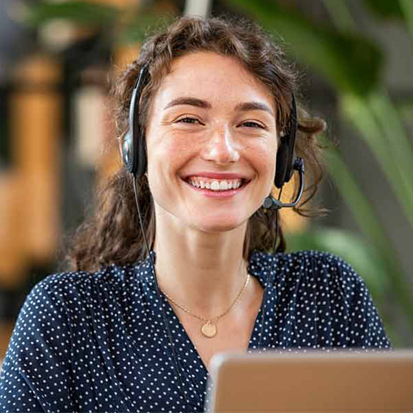 A happy woman wears a headset and sits in front of a laptop while working the IT Service Desk.