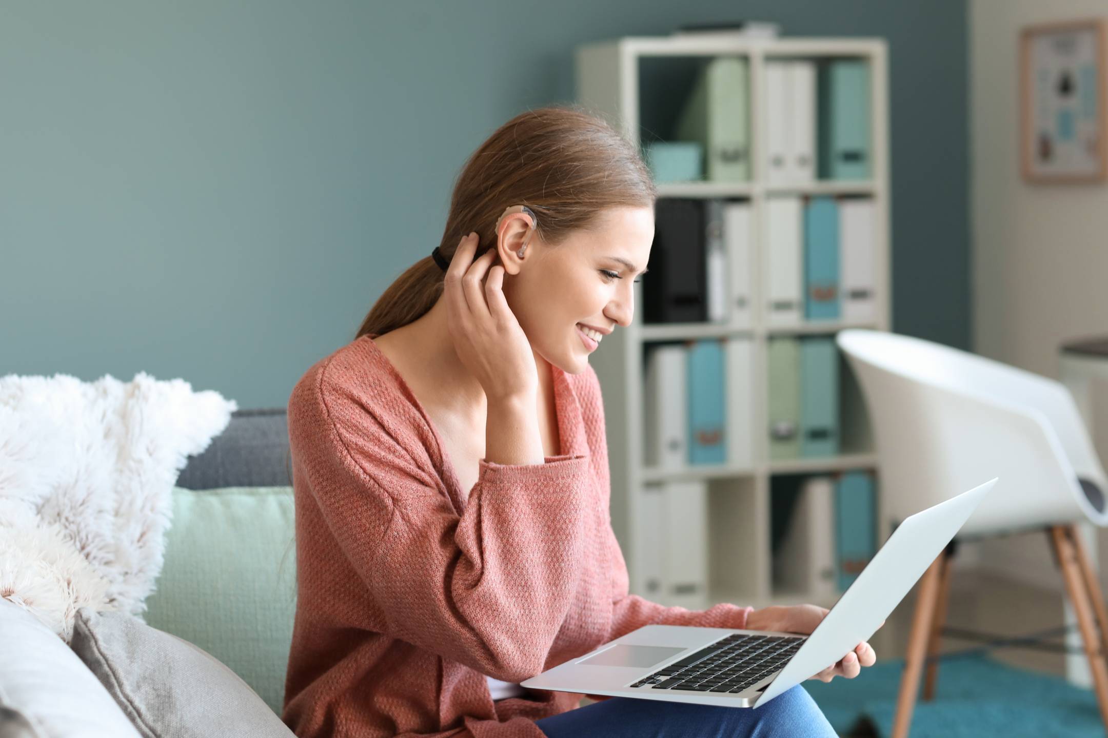 A happy woman with a hearing aid sits on a couch and uses her laptop to access North Dakota government services.