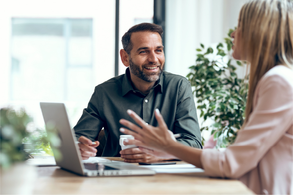 Two happy coworkers—a man and a woman—interact next to a laptop after joining North Dakota’s Microsoft Teams ADA chat.